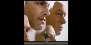 A picture of a presentation in front of a large image of men's faces