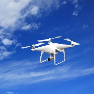 a white drone flying through a blue sky with clouds
