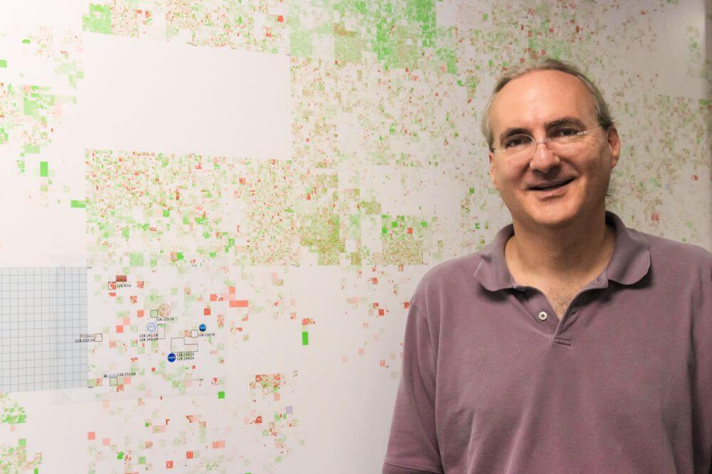 A photo of John Heidemann standing in front of a map depicting the whole internet address space, comprising 4.3 billion internet addresses, which was mapped by Heidemann and his team in 2011.