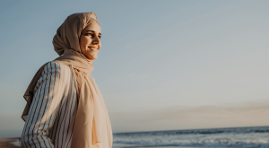 A woman in hijab smiling as she overlooks the sunset over the ocean.