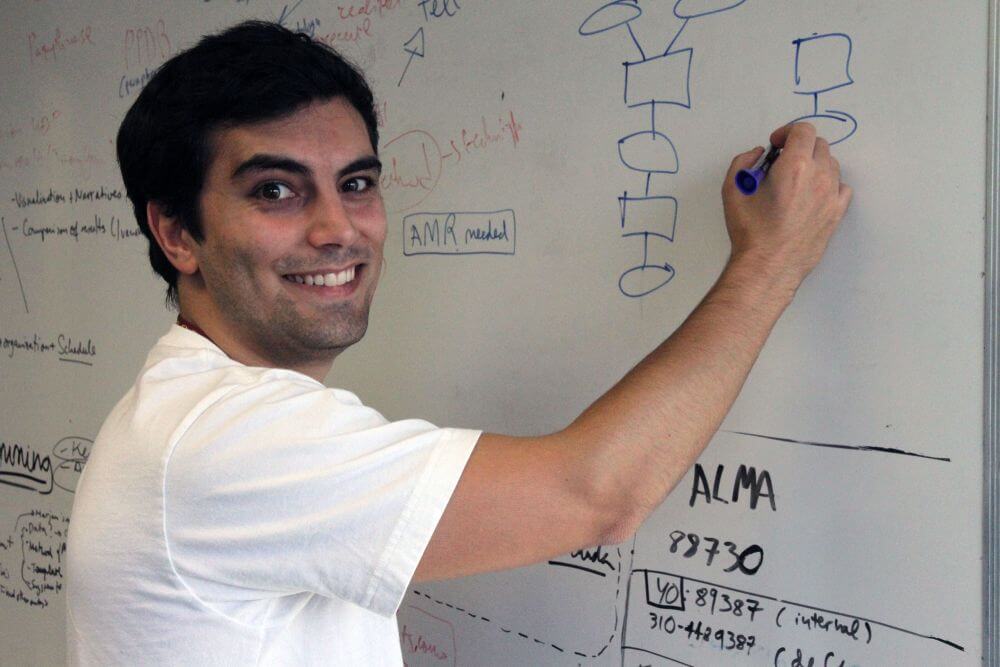 A photo of ISI's Daniel Garijo writing on a whiteboard and smiling