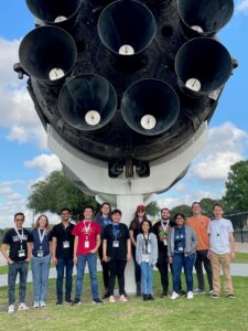 Team Aegis stands underneath one of the only two Falcon 9 boosters on display in the world, previously used in multiple missions to deliver supplies to the International Space Station.