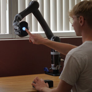 Lead author Nathan Dennler, a computer science doctoral student, with the robotic arm, which provides precise 3D spatial information, and a socially assistive robot, which gives instruction and motivation throughout the assessment. Photo/Nathan Dennler.