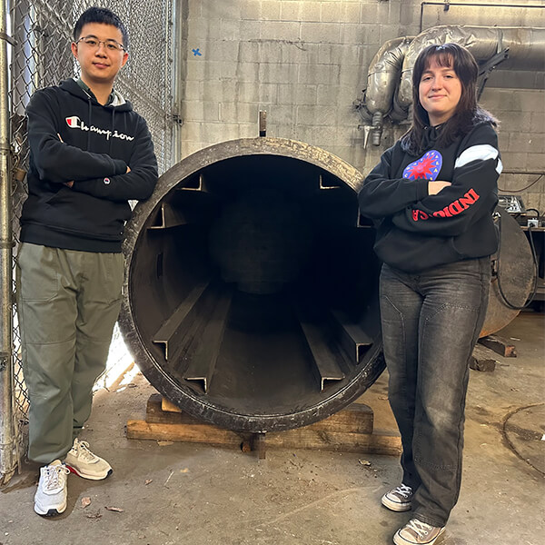 PhD students Bozhou Zhuang and Anna Arcaro in front of a research mock-up of a nuclear fuel canister