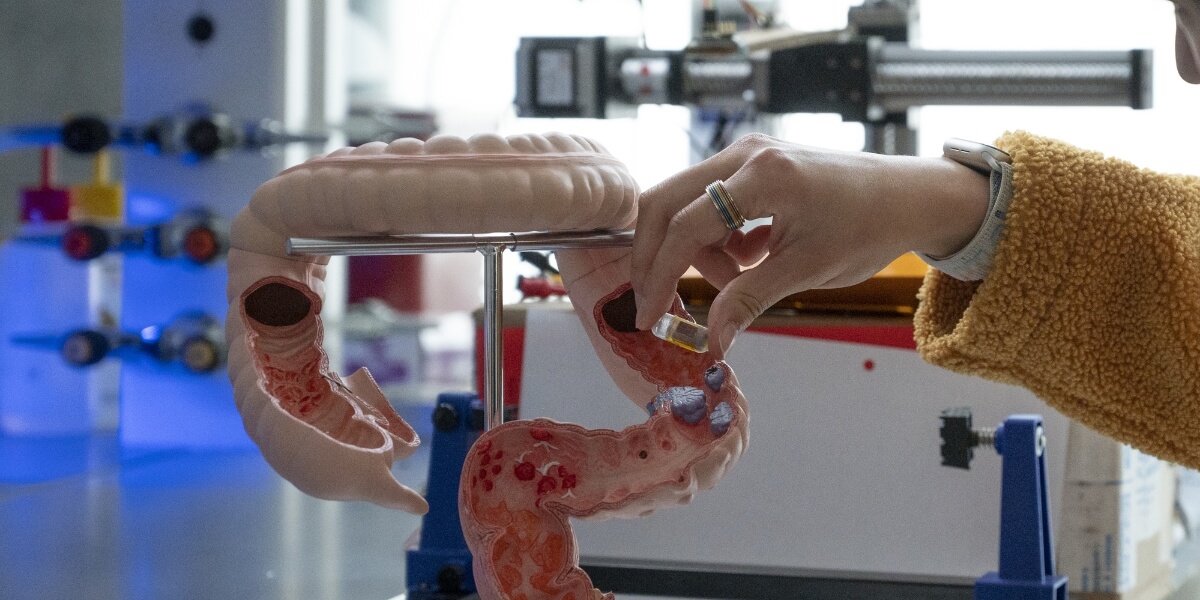 A person's hand is shown holding a smart sensor against a model of the intestine