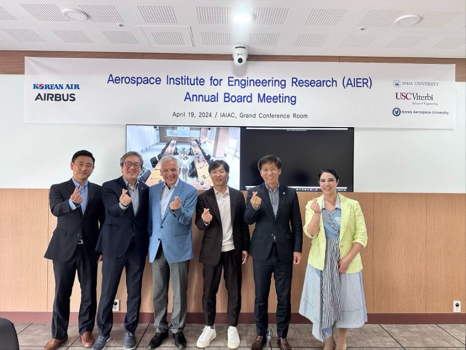 A group of six people standing in a conference room, smiling and making heart gestures with their fingers. A banner above them reads 'Aerospace Institute for Engineering Research (AIER) Annual Board Meeting' with logos of Korean Air, Airbus, Inha University, USC Viterbi School of Engineering, and Korea Aerospace University. The date is April 19, 2024, and the location is IAIAC, Grand Conference Room.