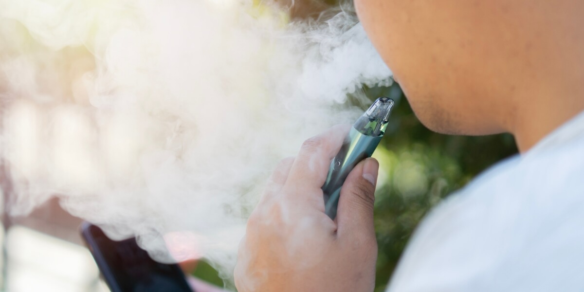 Smoke bellows out from a human mouth, the person is smoking a vaping pipe