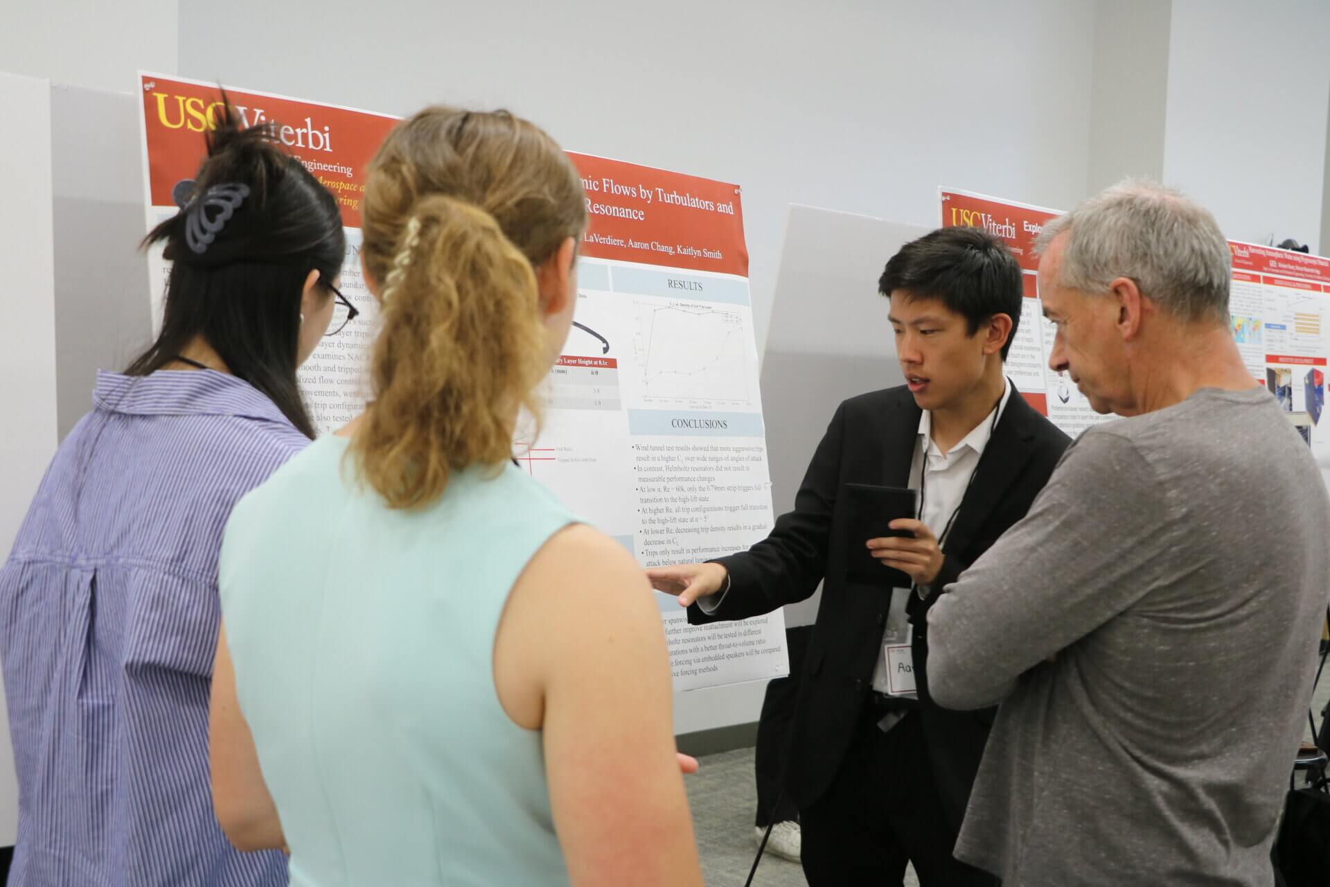 A student stands next to a research poster, explaining their project to attendees